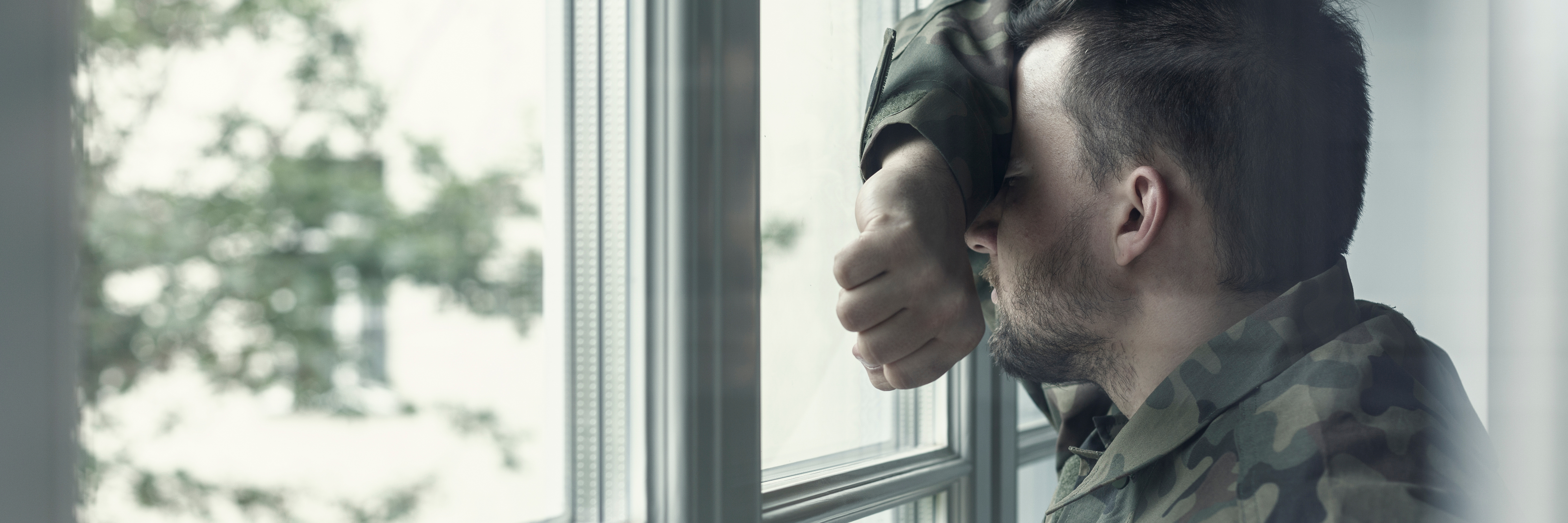 Man standing at window hiding face with his arm
