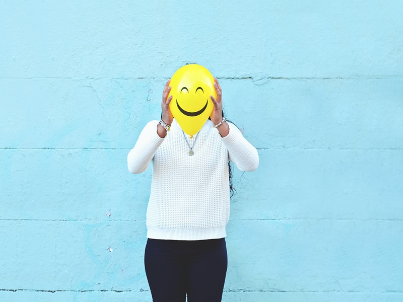 Someone holding a balloon with a happy face in front of their own face