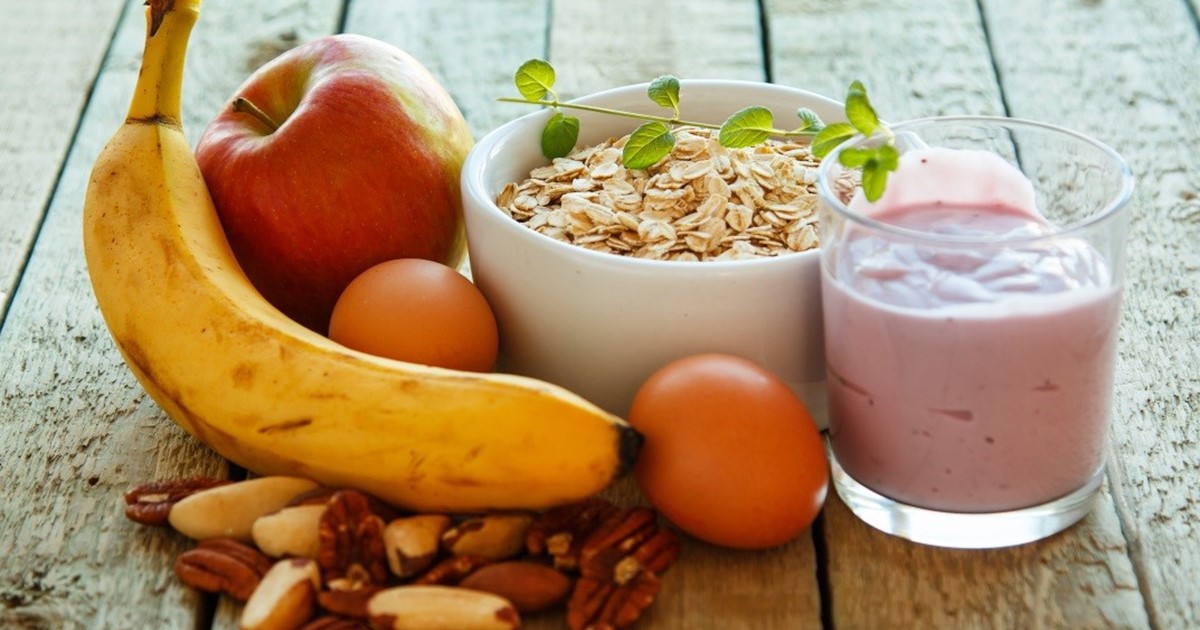 Picture of a banana, fruit smoothie, bowl of cereal, apple, satsumas and nuts