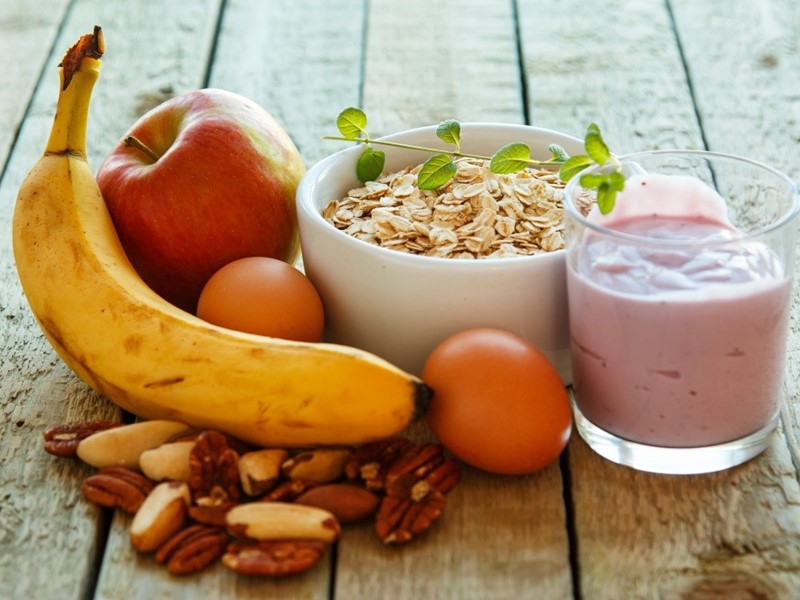 Picture of a banana, fruit smoothie, bowl of cereal, apple, satsumas and nuts